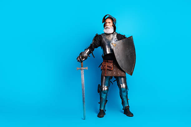 istock Elderly knight in full medieval armor holding a sword and shield against a vibrant blue background 2215837666