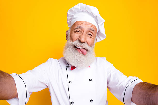 istock Senior chef with a playful expression in white uniform on a yellow background 2215839316