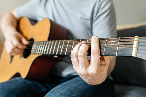 istock Man sitting and playing guitar, strumming chords, learning to play. Hobbies for adults 2215840081