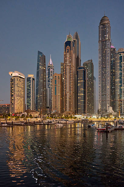 Illuminated skyscrapers against sky at night. Tall business buildings in city. Futuristic towers near sea in downtown.