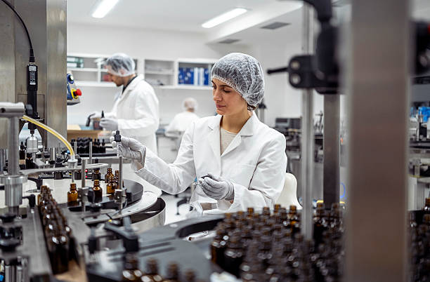 istock Laboratory Worker In White Coat And Hairnet Inspecting Products On Pharmaceutical Production Line 2215843106