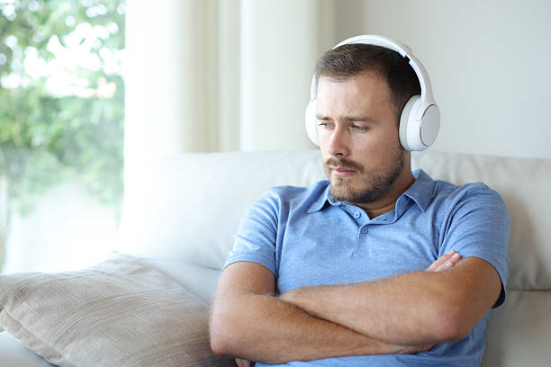 Neurodiverse beautiful young woman with ADHD wearing headphones is taking a break sitting by the window and listening relaxing music. Peaceful moments in quiet place.