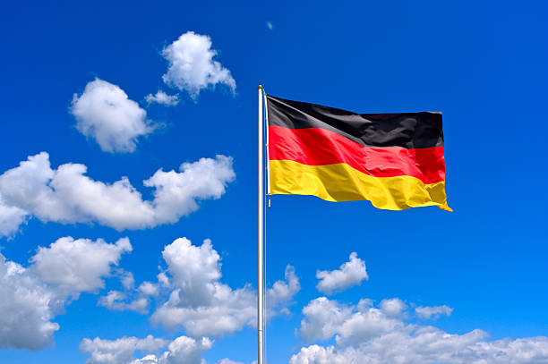 The flag of  Germany flutters in the wind in a blue sky with white clouds