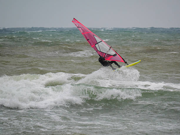 istock Water Sport Activity - Windsurfer Riding a Wave in Rough Sea on a Windy Day 2215843475