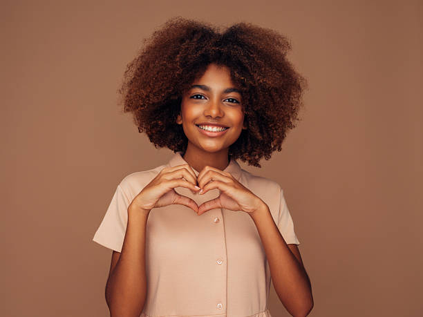 istock Smiling woman making a heart gesture against a neutral background 2215844253