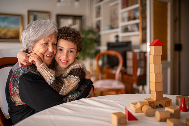 Grandchild hugging grandmother, smiling and having fun together at home while playing with building blocks