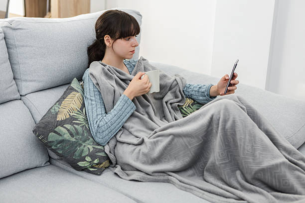 istock Cozy woman using smartphone while sipping coffee at home in a blanket 2215848401