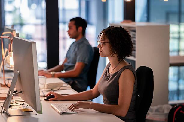 istock Professionals Working at Modern Office Desks with Computers and Cozy Lighting During Focused Collaboration 2215850909