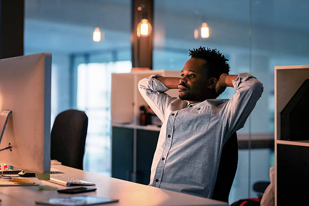 istock Modern Office Scene with a Relaxed Professional Reflecting at a Computer Desk in the Evening 2215851468