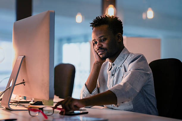 istock Focused Young Man Working Late at an Office Desk in a Dimly Lit Workspace with Modern Equipment 2215851480