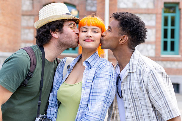 Two friends kissing a girl on the cheeks at the same time Two male friends kissing a female friend on her cheeks at the same time, showing affection and friendship three way kiss stock pictures, royalty-free photos & images