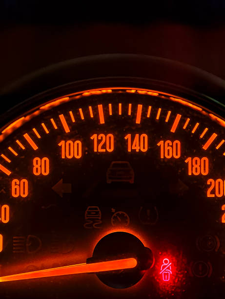 A detailed view of a car speedometer illuminated with bright orange lights, various dashboard indicators
