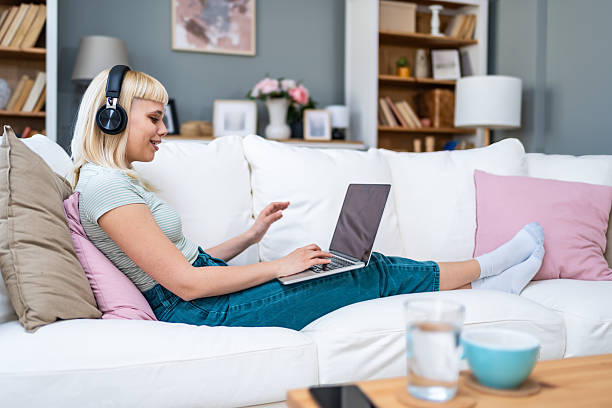 istock Young woman exchange student sitting on sofa at home using laptop with wireless headphones for remote work attending virtual classes video meetings, studying, writing, editing, researching, presenting 2215861470