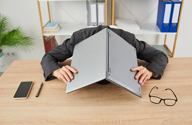 istock Stressed, tired man lays his head on office working desk and covers it with laptop 2215863291