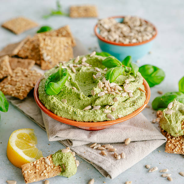 Small bowl filled with green vegan dip/spread decorated with sunflower seeds and fresh basil