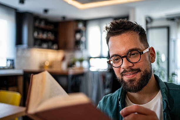 istock Young man reading a book and smiling in his modern apartment 2215865219