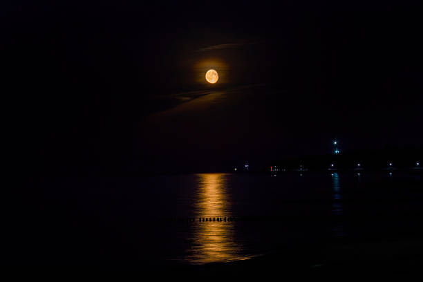 istock Calm ocean at sunset. Bright moon rises in the sky. Moon path on the waves. 2215868202
