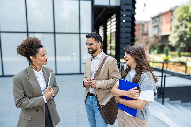 istock Diverse team of corporate professionals in formal attire collaborating outdoors, engaged in strategic discussion while analyzing data on laptop in front of modern glass office building. 2215870208