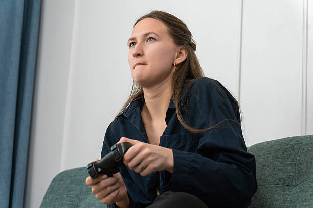 istock Young woman sitting on a comfortable sofa, holding a gamepad and playing video games, concentrating on the action and enjoying her leisure time in a cozy home environment 2215873129