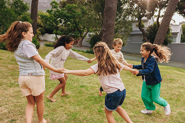 Group of children holding hands and playing outdoors in a green park. A joyful scene of fun, friendship, and leisure under bright sunlight.