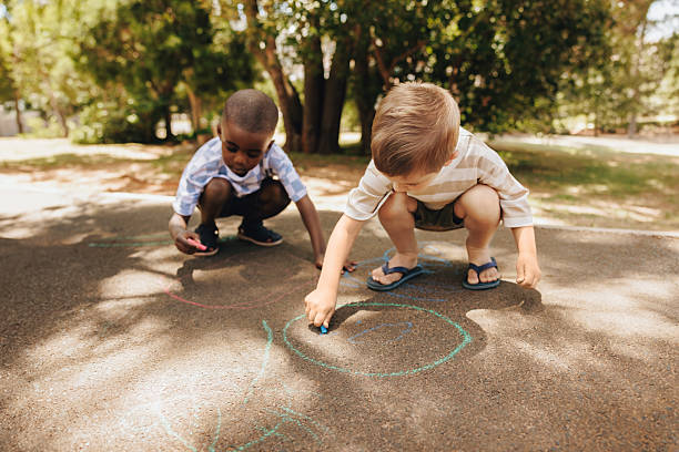 Children drawing with chalk on sidewalk in sunny outdoor park setting