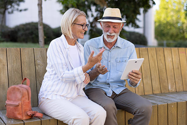 istock Joyful elderly couple using a tablet on a wooden bench in park 2215894693