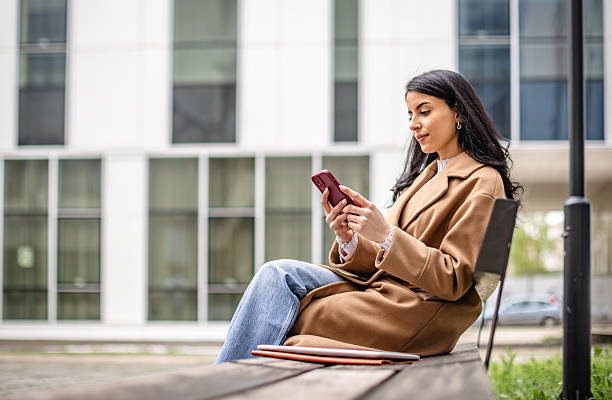 istock Businesswoman enjoying a break while using her phone outdoors near a modern corporate building surrounded by greenery 2215906402