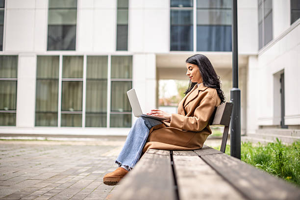 istock Businesswoman working outdoors on a laptop while seated on a bench in a modern office environment during a sunny day 2215912730