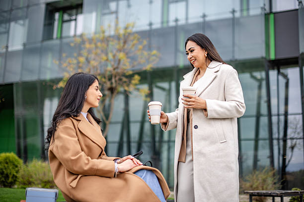 istock Businesswomen engage in conversation while enjoying coffee outside a modern office building during daytime 2215913338