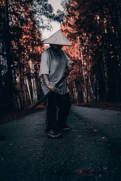 istock A warrior stands on a path in the forest, holding a katana in both hands. He wears a straw hat and dark clothes. The samurai warrior stands in a fighting stance and is ready to repel any attack. 2215914669