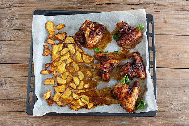 chicken wings and potatoes on baking sheet, roasted together, on wooden background, seen from above