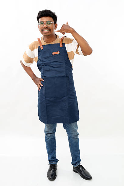 istock Asian young man wearing apron over white background smiling doing phone gesture with hand and fingers like talking on the telephone. communicating concepts. 2215916033