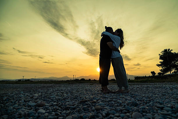 Couple embraces on a rocky path during a beautiful sunset, showcasing love and togetherness