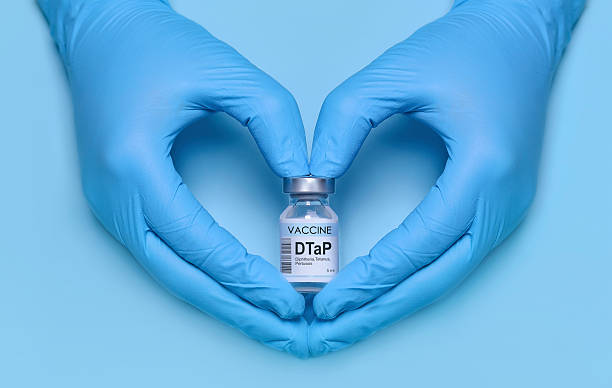 istock Doctor's gloved hands forming a heart shape while holding a DTaP vaccine vial on a blue background, symbolizing protection, care, immunization, and healthcare awareness. Banner with copy space 2215921643