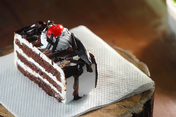 Close-up of a rich black forest pastry slice with whipped cream and cherry on top, styled on a rustic background. Perfect for dessert and bakery concepts.