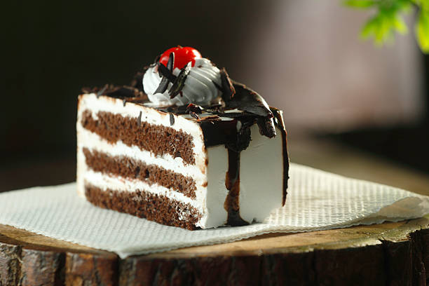Close-up of a rich black forest pastry slice with whipped cream and cherry on top, styled on a rustic background. Perfect for dessert and bakery concepts.