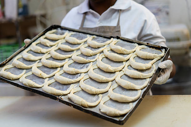 Female baker hands holding a baking tray with croissant.  Baker working in commercial bakery preparing fresh croissant.