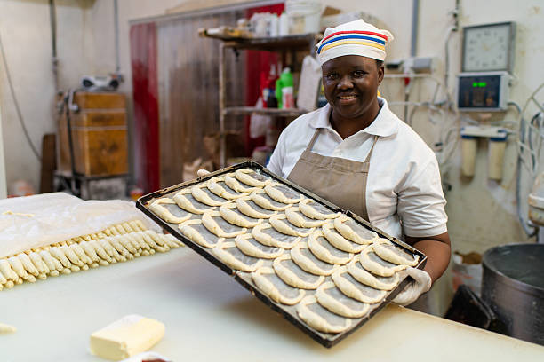 Happy woman baker holding a baking tray with croissant.  Baker working in commercial bakery preparing fresh croissant.