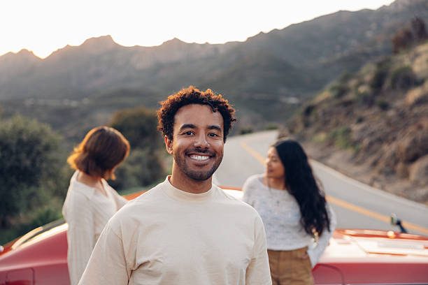 Man smiling during a road trip traveling Southern California with a vintage car on coastal winding roads.