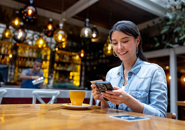 istock Woman at a restaurant making a payment on her phone using her credit card 2215931020