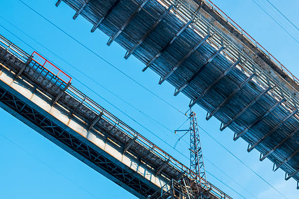 A bridge with a metal railing and a wire running across it. The bridge is blue and the sky is clear
