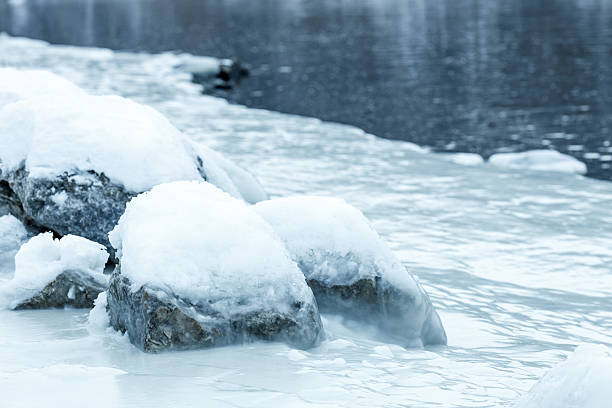 istock A rock covered in snow sits in the water 2215932335