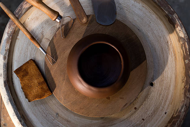 A potter's wheel with a clay pot on top of it. The potter's tools are laid out on a wooden board