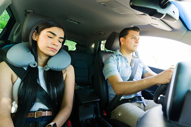 istock Young man driving car while girlfriend sleeps with travel pillow 2215935455