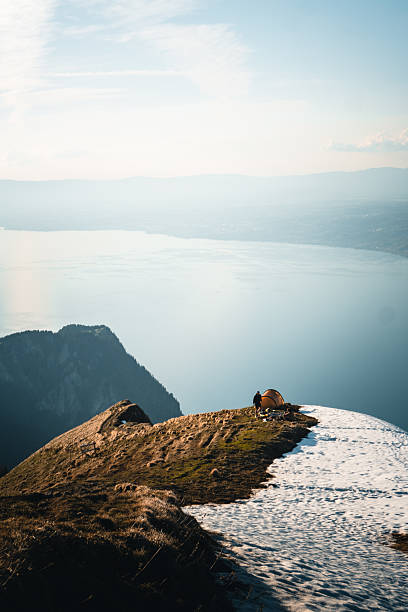 Young men enjoy sunrise from campsite on mountain peak above lake Geneva and distant mountains, distant view, Mount Grammont, Valais, Swiss Alps