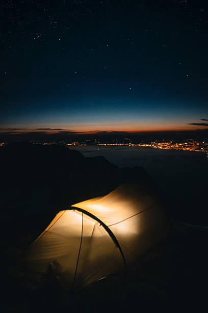 istock Illuminated tent at campsite on mountain peak above lake 2215939325