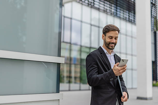istock Smiling Businessman Checking Phone Outside Office Building 2215940468