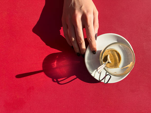 Woman's hand resting beside an empty glass coffee cup and saucer on a vibrant red table, capturing the essence of a completed coffee break moment filled with relaxation