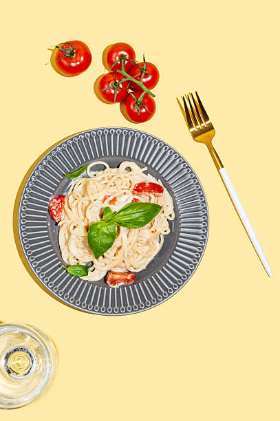 istock Creamy spaghetti with tomatoes, cheese and basil on a plate on a yellow background 2215953745