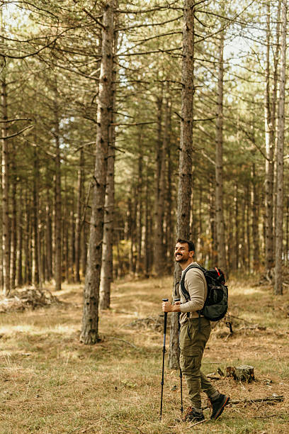 istock Smiling male hiker exploring forest trail with backpack and trekking poles 2215955717
